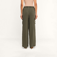A woman stands facing away, wearing the Chandler Cargo Pant in olive green, styled with a beige top. These wide-leg cargo pants feature an elastic waistband and side pockets as she poses against a plain white background.