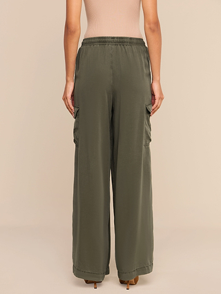 A person wearing the Chandler Cargo Pant in loose olive green, paired with a beige top and standing with their back to the camera against a plain beige background.