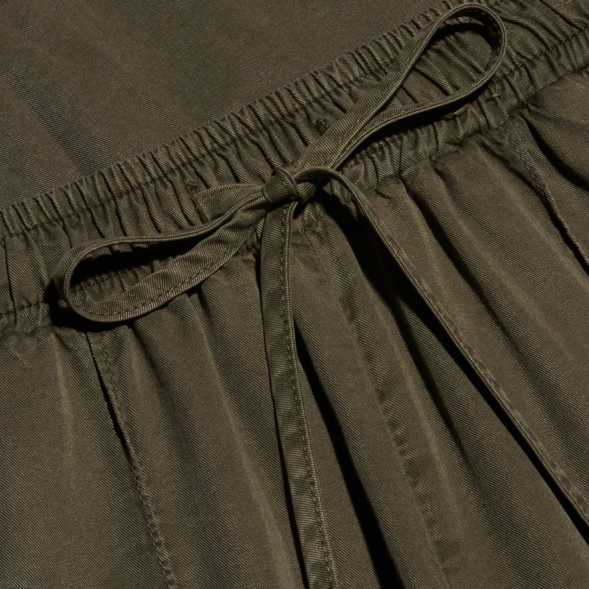 Close-up of the Chandler Cargo Pant in olive green, featuring an elastic waistband with a tied drawstring bow at the center. The lightweight fabric has a slightly textured appearance.