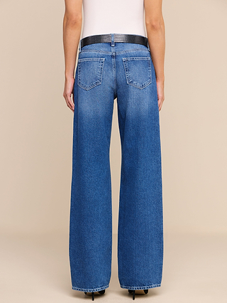 A person is shown from the back against a plain beige background, wearing the Christel Wide-Leg Jean in high-waisted, wide-leg blue all-cotton denim, paired with a black belt and a white top.
