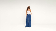 A woman wearing a white tank top, dark sunglasses, and blue wide-leg jeans with a folded waistband.