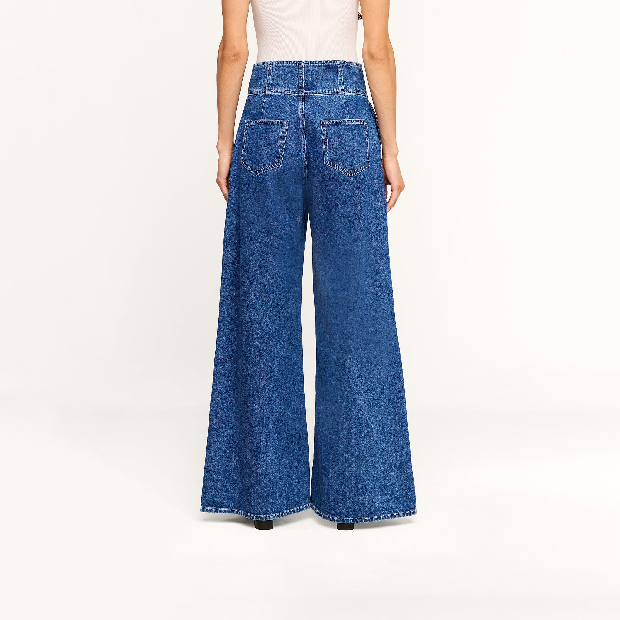Model wearing the Sonja Corset Jean, featuring an ultra high-rise fit and wide-leg silhouette, paired with a white top. Shown from the back against a plain white background, the jeans showcase two large back pockets and a high waist.