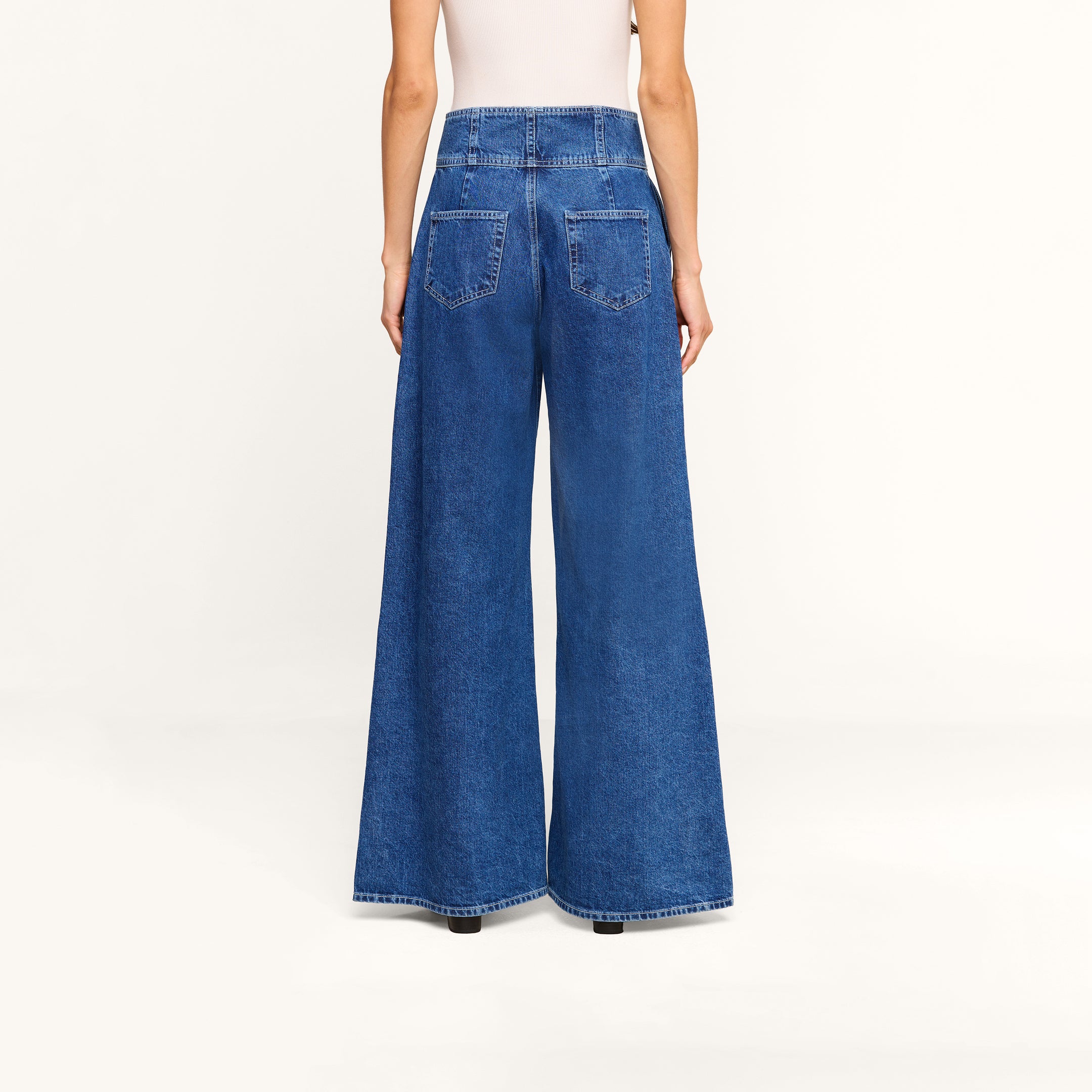 Model wearing the Sonja Corset Jean, featuring an ultra high-rise fit and wide-leg silhouette, paired with a white top. Shown from the back against a plain white background, the jeans showcase two large back pockets and a high waist.