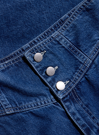 Close-up of blue denim fabric with visible white stitching and three silver buttons aligned in a row, showcasing the refined details and contemporary silhouette of the Sonja Corset Jean.
