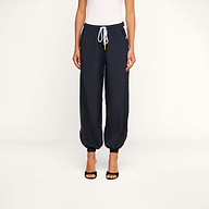 A person wearing a white sleeveless top, the Mariko Jogger—a pair of dark lightweight nylon jogger pants with zippered pockets—and black open-toe heels stands against a plain white background.