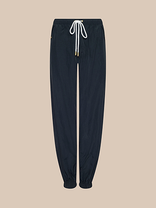 The Mariko Jogger in black features an elastic waistband, a white drawstring, and elastic cuffs. Crafted from lightweight nylon with a water-repellent finish, it is displayed on a beige background.