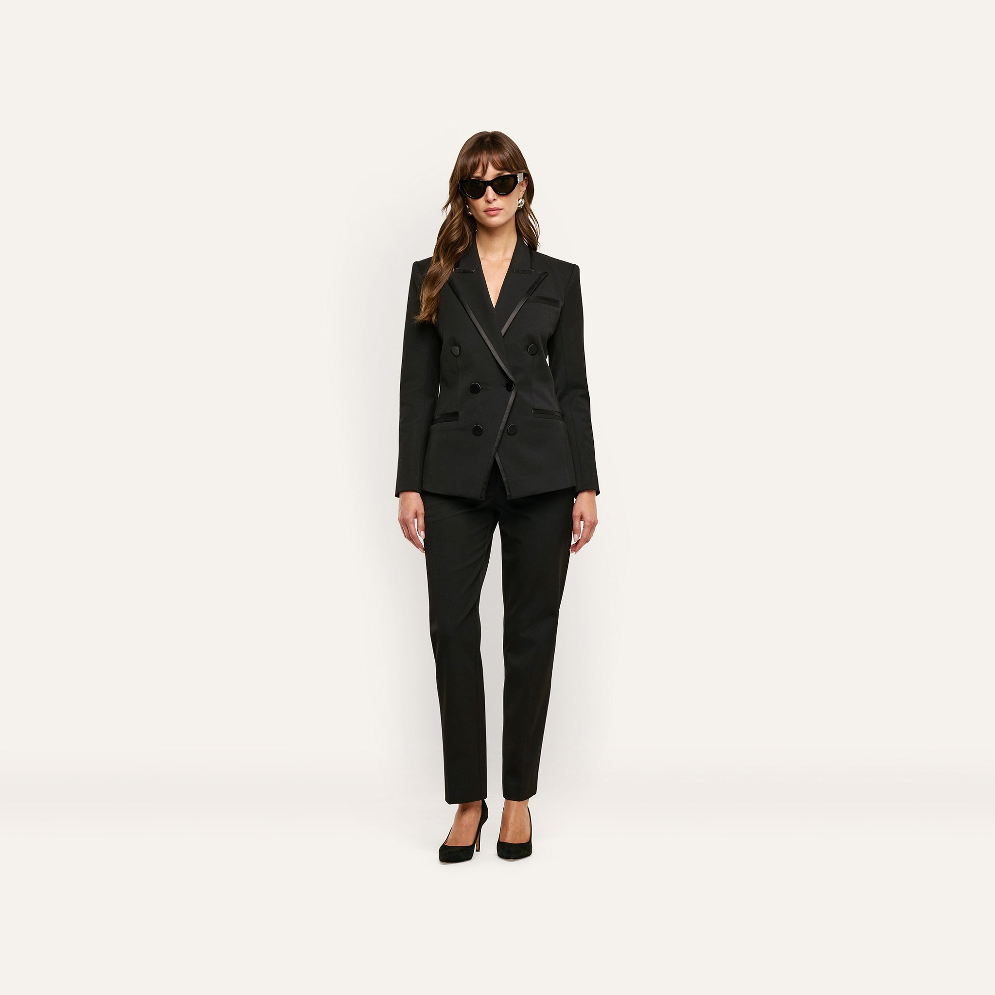 A person wearing a black double-breasted blazer with satin lapels, matching Rebel Trouser slim-straight trousers, and black high heels.