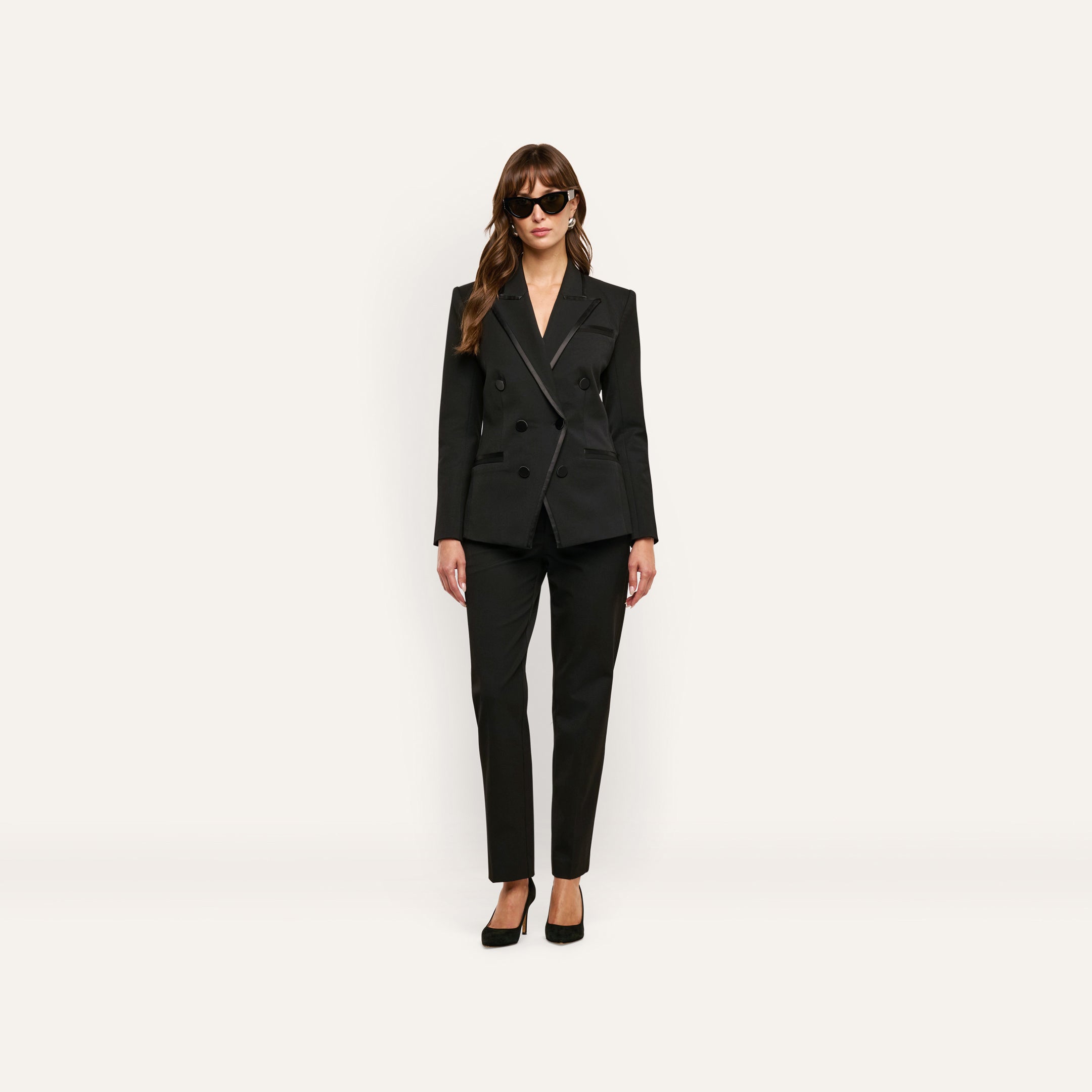 A person wearing a black double-breasted blazer with satin lapels, matching Rebel Trouser slim-straight trousers, and black high heels.