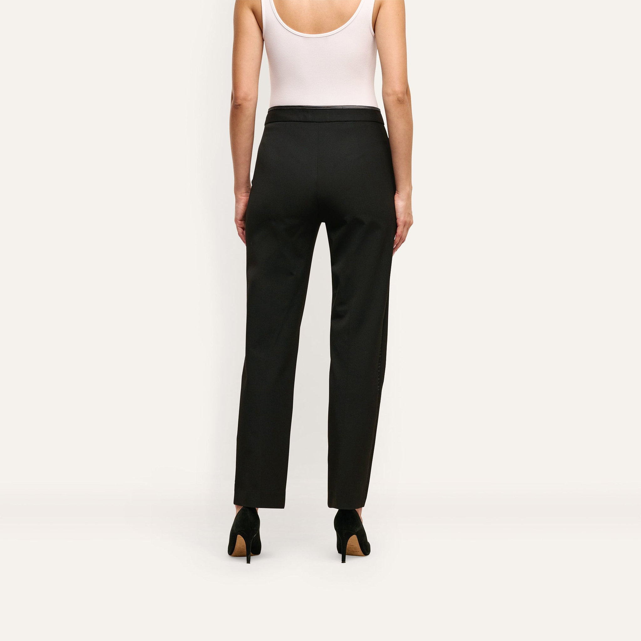A person viewed from behind wearing slim-straight, black stretch twill Rebel Trouser suiting trousers and black high-heeled pumps.
