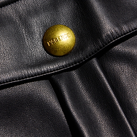 Close-up of a black vegan leather cargo pocket flap on the Clairmont Vegan Leather Short, secured by a large, round brass button embossed with the brand name.