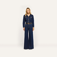A woman wearing a dark wash denim jacket and matching Jules Wide-Leg Jean with high-rise, wide-leg styling and gold-tone hardware.
