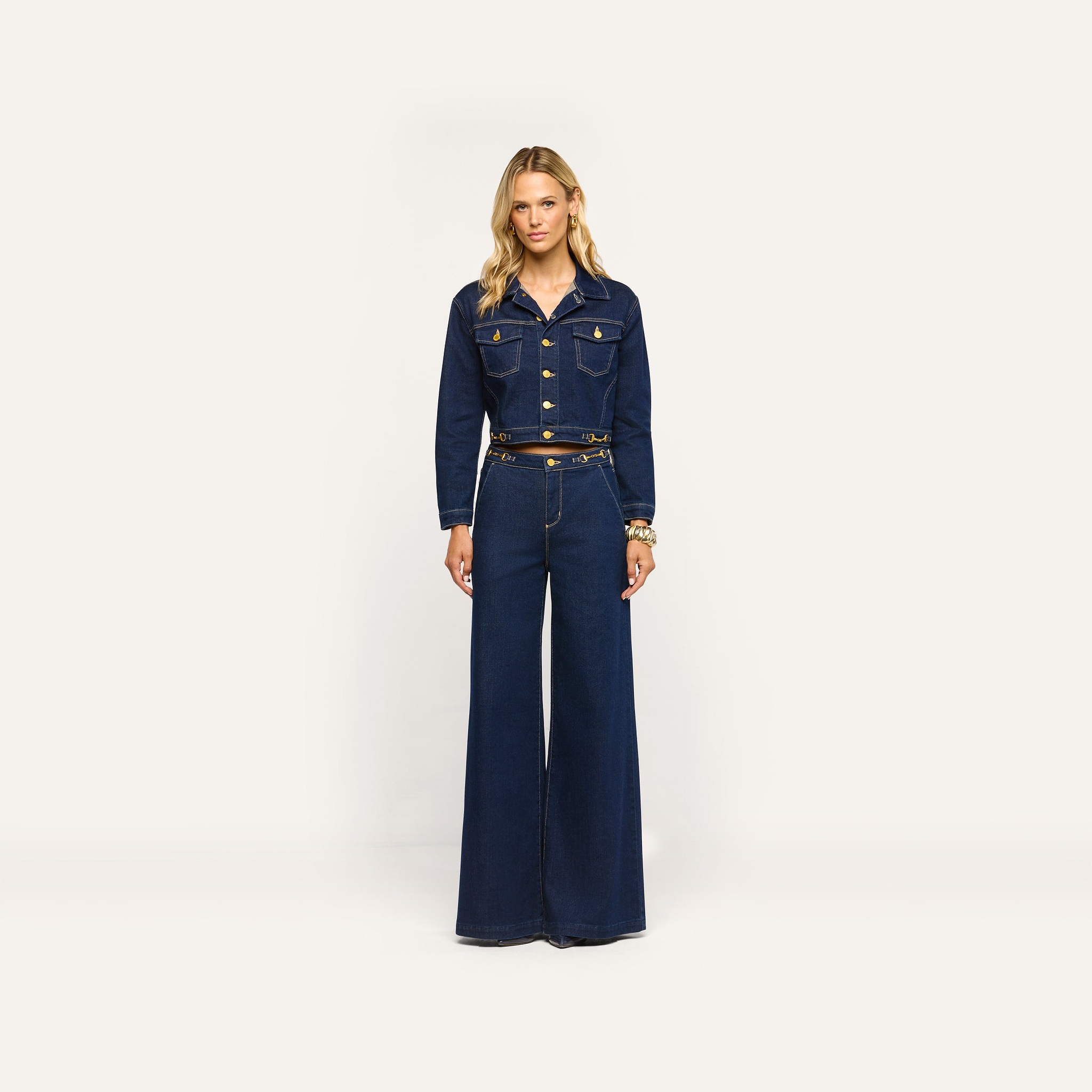 A woman wearing a dark wash denim jacket and matching Jules Wide-Leg Jean with high-rise, wide-leg styling and gold-tone hardware.
