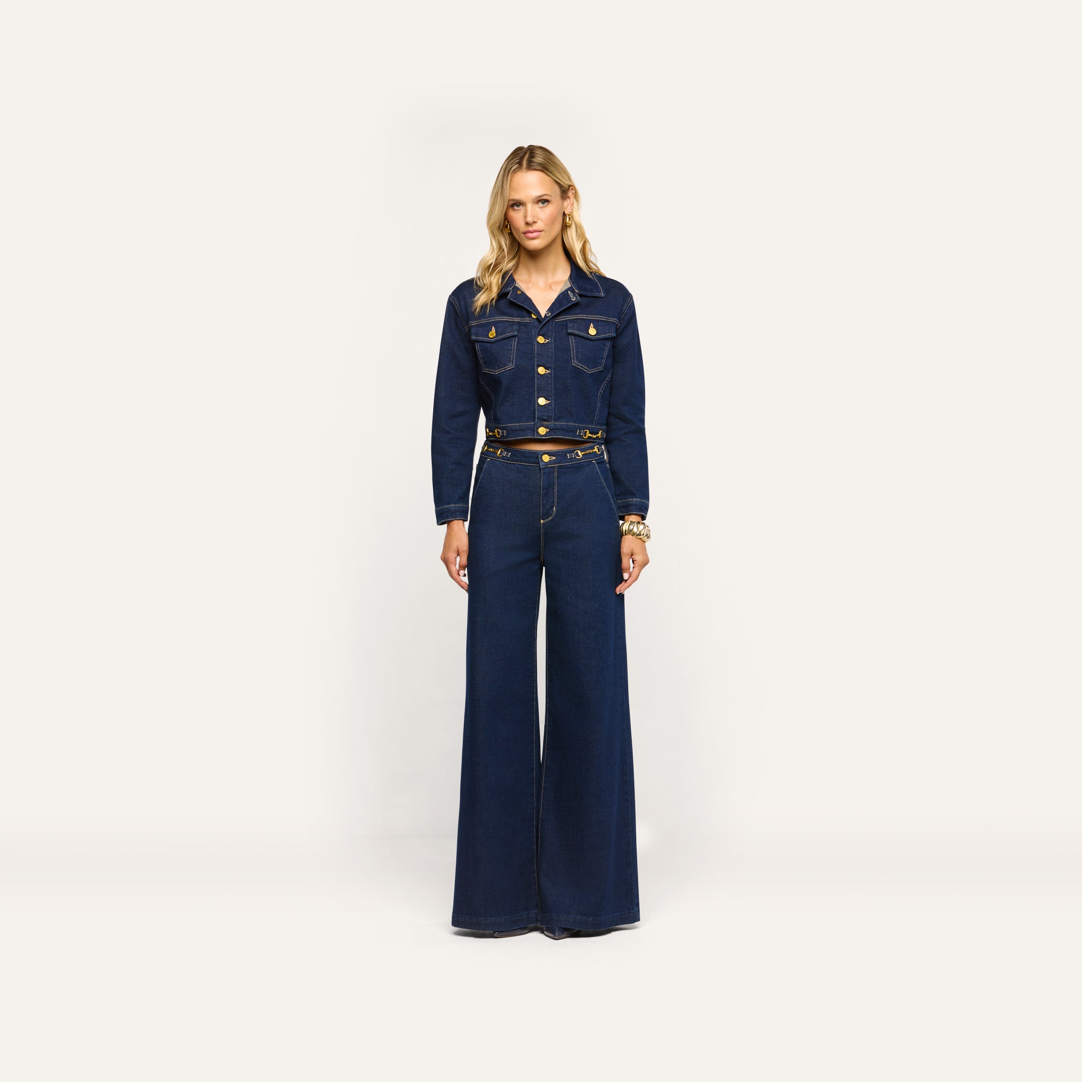 A woman wearing a dark wash denim jacket and matching Jules Wide-Leg Jean with high-rise, wide-leg styling and gold-tone hardware.