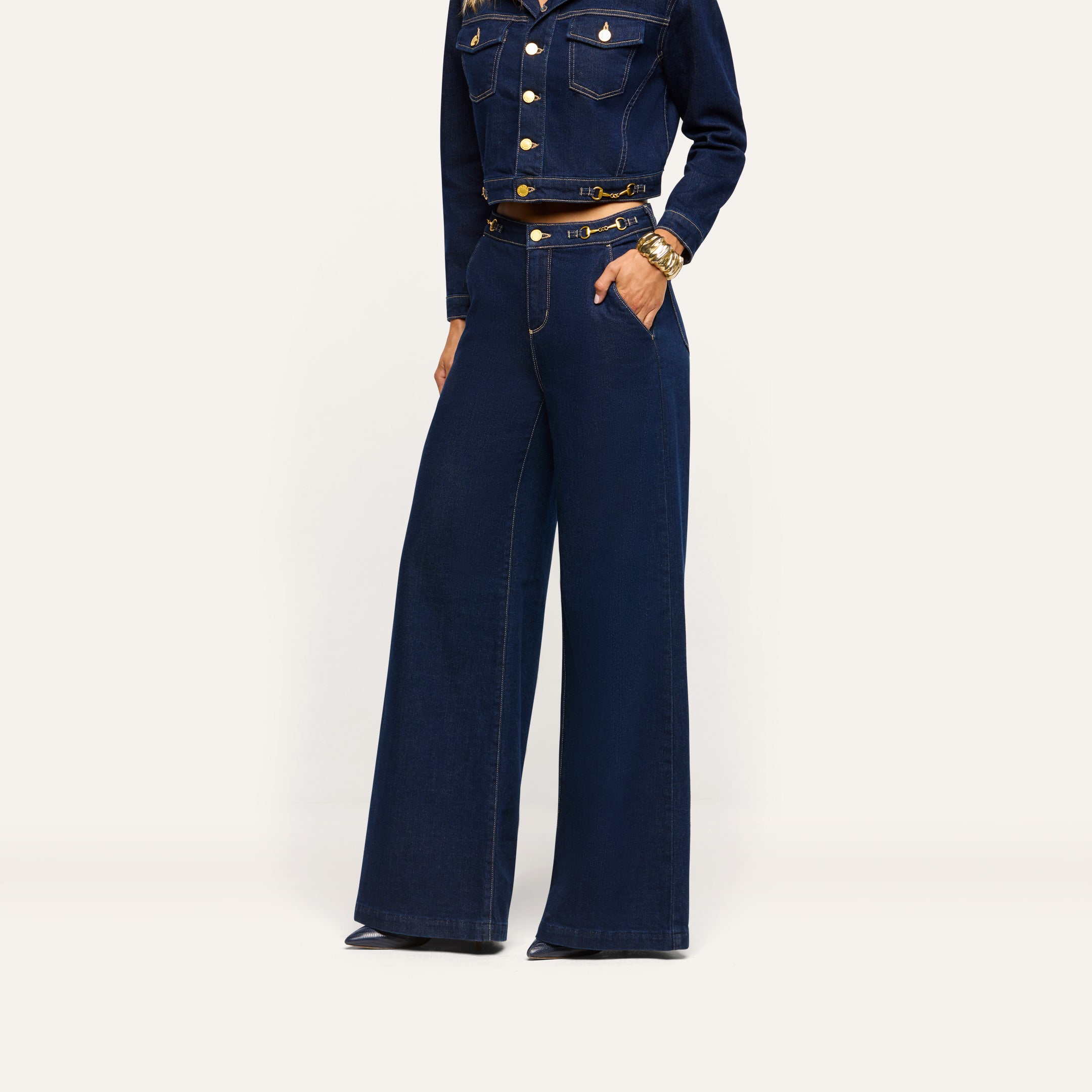 A person wearing a cropped dark-wash denim jacket and matching Jules Wide-Leg Jean with gold-tone horsebit hardware at the waist.