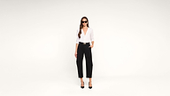 A woman with long hair wears sunglasses, a white blouse, black high-waisted pants, and black heels, standing confidently against a plain white background.