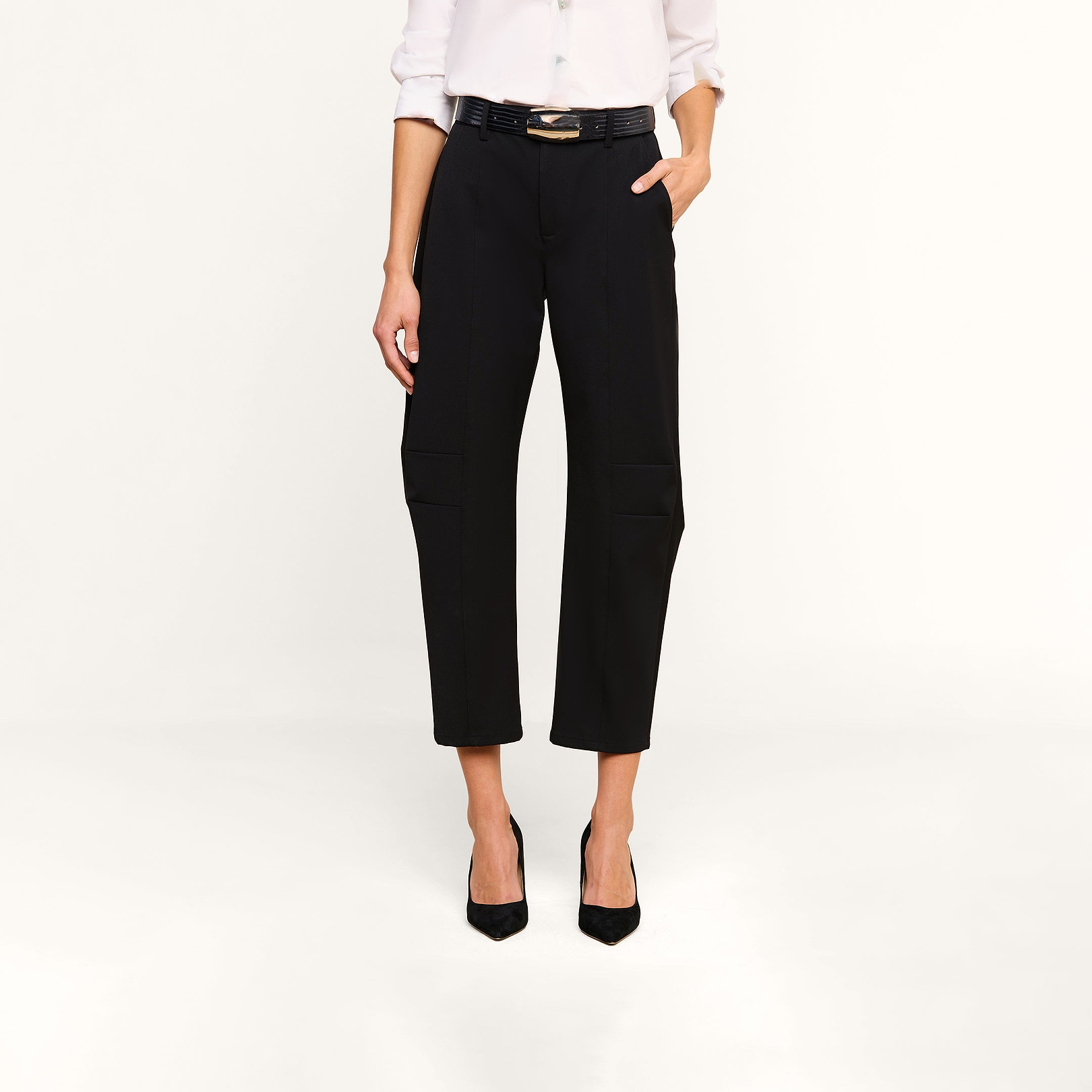 A person stands against a beige background with one hand in their pocket, wearing the Colby Barrel-Leg Trouser in black, styled with a white long-sleeve shirt and black heels.