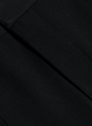 Close-up of black fabric with a smooth texture and visible stitching, from the Colby Barrel-Leg Trouser, showing intersecting seams and folded sections.