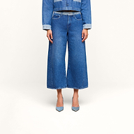Eine Person trägt eine blaue Jeansjacke mit hochgekrempelten Ärmeln, dazu eine „Bronte Cropped Wide-Leg Jeans“ mit hohem Bund. Zu sehen ist nur der Oberkörper von den Schultern bis zu den Füßen; das Outfit wird durch hellblaue Pumps mit spitzer Zehenpartie abgerundet.