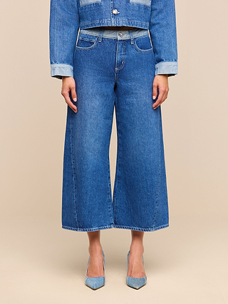 A person is wearing a blue denim jacket with the cuffs rolled up on the sleeves, paired with Bronte Cropped Wide-Leg Jeans that feature a high waistband. Only the body from shoulders to feet is visible, and the outfit is completed with light blue pointed-toe heels.