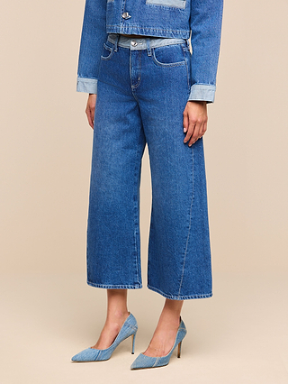 A person wearing Bronte Cropped Wide-Leg Jean in blue, styled with a matching denim jacket and blue high-heeled shoes, stands against a beige background with their face not visible.