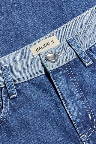 Close-up of the Bronte Cropped Wide-Leg Jean in blue denim, featuring a prominent silver button, belt loops, and a white label above the high waistband displaying “PAGENCE” in bold black uppercase lettering. The cropped wide-leg silhouette lends a contemporary update to this timeless style.
