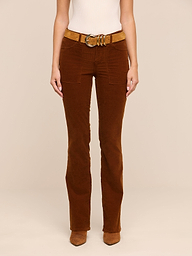 Model showcases the lower half of their body wearing the Saffia Corduroy Pant in brown, styled with a tan belt and brown shoes, posed against a plain white background.