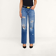 A person wearing the Zelda Slouchy Straight Jean in a destructed, ripped blue denim style, paired with a black top, a black belt with a gold buckle, and black heels stands against a plain white background.