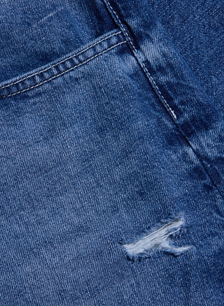 Close-up of the Zelda Slouchy Straight Jean in a medium indigo wash, featuring a pocket, softly faded fabric, and a small rip with frayed edges near the bottom right—perfectly highlighting their signature slouchy-straight silhouette.