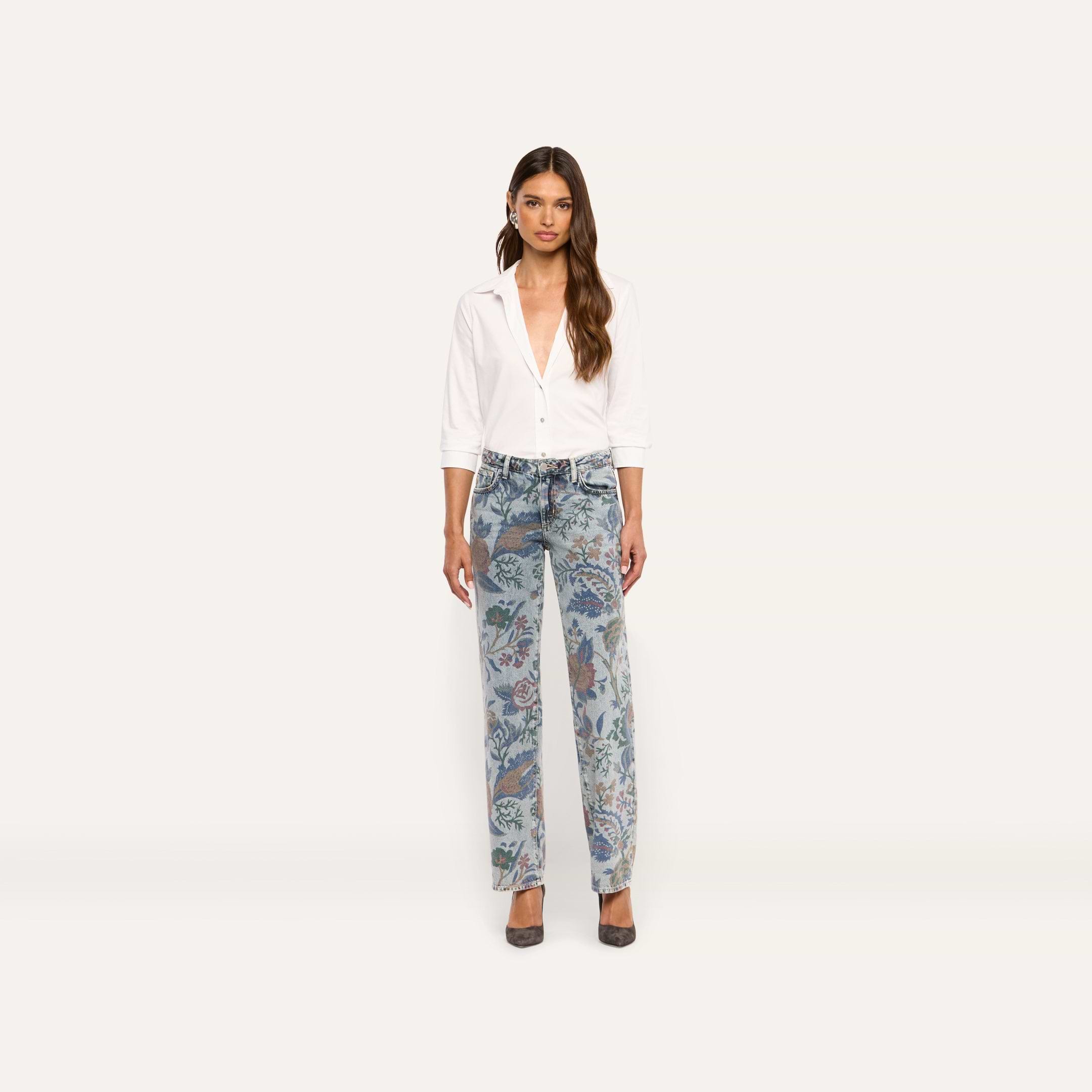 A woman wears a white button-down shirt tucked into Gianna Stovepipe Jean low-rise, slim jeans featuring an intricate, multicolored floral print.