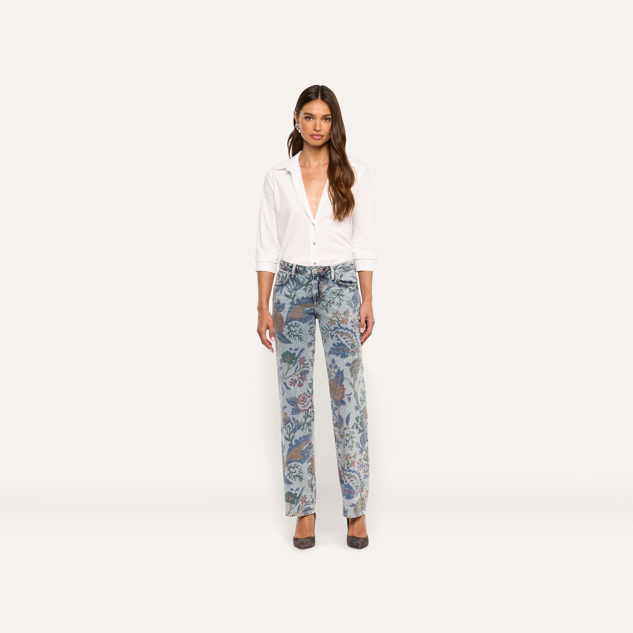 A woman wears a white button-down shirt tucked into Gianna Stovepipe Jean low-rise, slim jeans featuring an intricate, multicolored floral print.