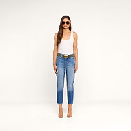 A woman stands against a plain white background, facing forward with her arms relaxed at her sides, wearing sunglasses, a white tank top, clear heels, and the Avena Slim-Leg Jean with a belt.