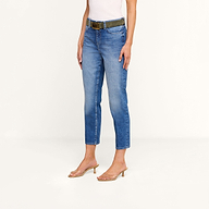 A person wearing the Avena Slim-Leg Jean in denim blue, a dark belt, a white sleeveless top, and clear heeled sandals stands against a plain, light background.