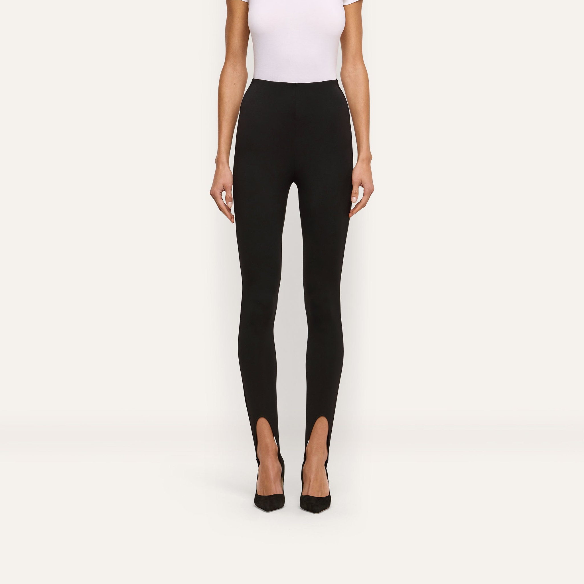A person wearing black Enid Stirrup Leggings in a high-waisted scuba knit fabric paired with black pointed-toe heels.