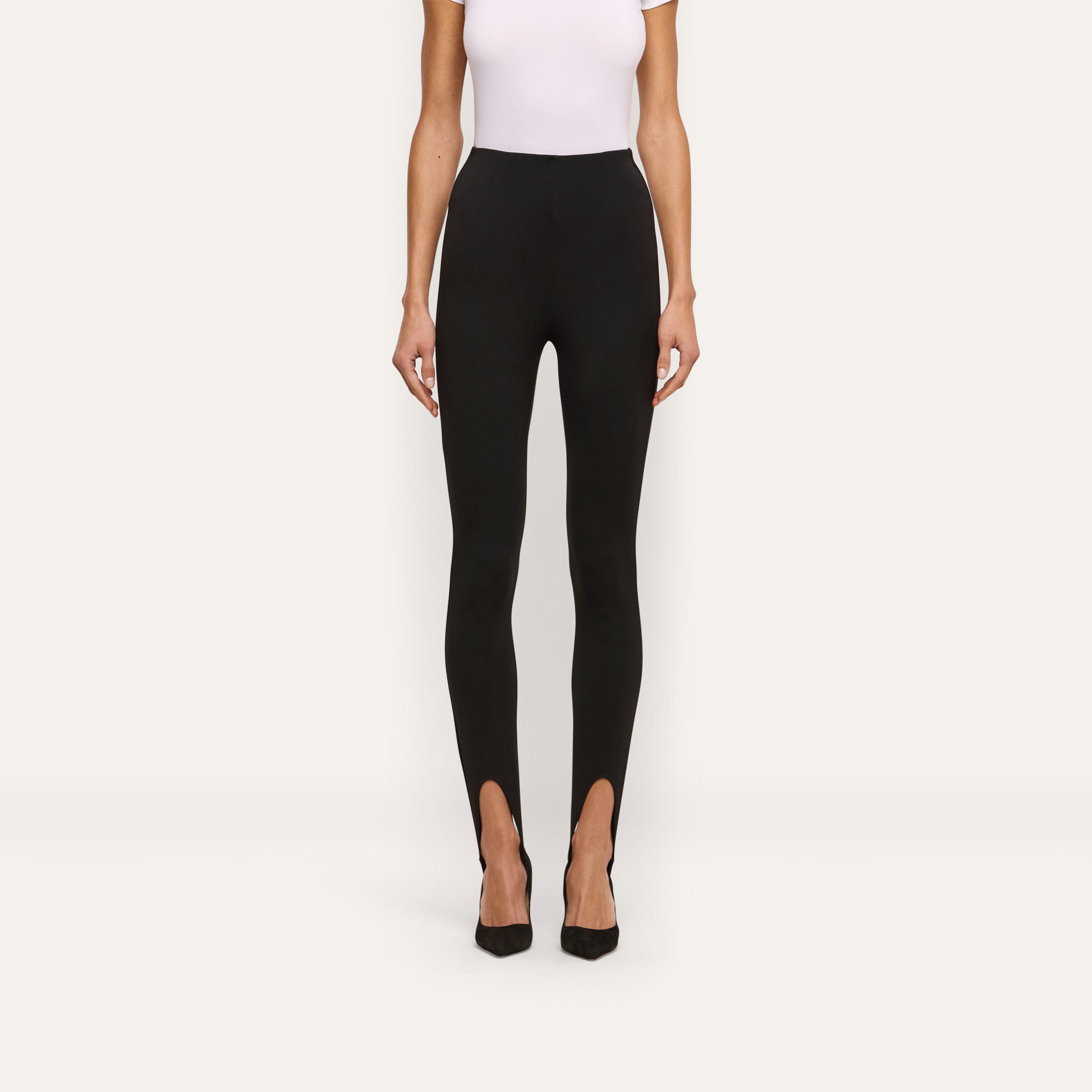 A person wearing black Enid Stirrup Leggings in a high-waisted scuba knit fabric paired with black pointed-toe heels.
