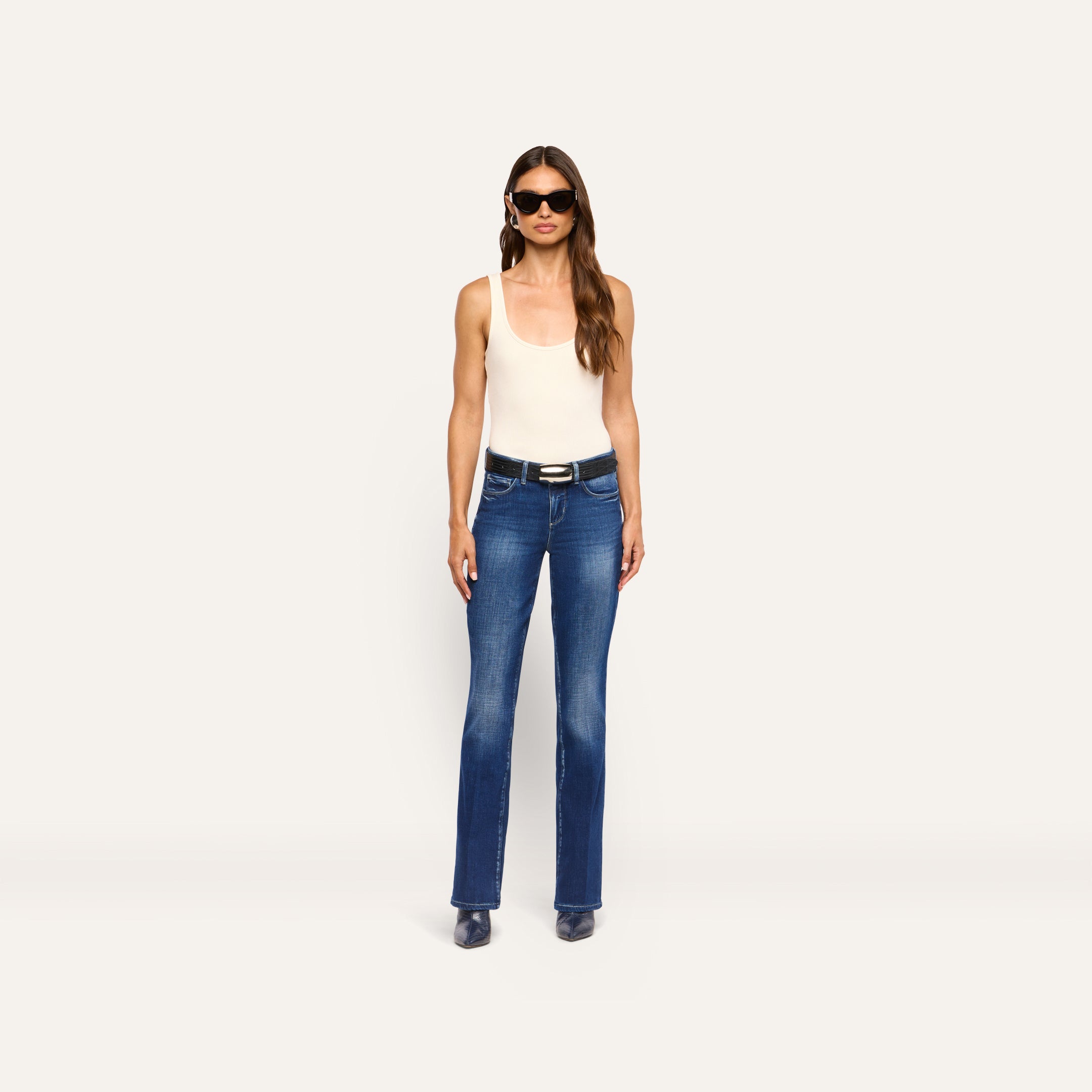 A person wearing a white tank top, a black belt, and Kezia Bootcut Jean low-rise stretch denim jeans.