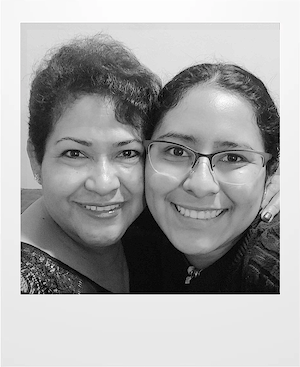 Two women smiling closely together for a selfie. One wears glasses and a necklace, while the other has short curly hair. The image is in black and white.