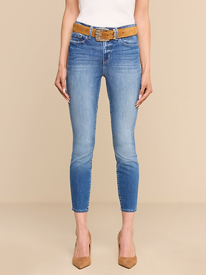 A person wears the Margot Cropped Skinny Jean in light blue premium stretch denim, styled with a tan belt, white top, and tan pointed-toe heels, standing against a plain beige background.