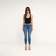 Una donna con occhiali da sole, un top nero senza maniche, i jeans Margot Cropped Skinny in lavaggio vintage, con una cintura color cuoio e tacchi dello stesso colore, è in piedi di fronte alla fotocamera su uno sfondo beige a tinta unita.