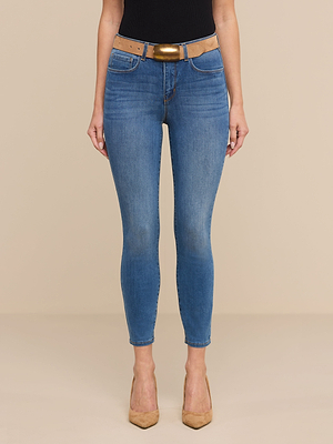 Wearing Margot Cropped Skinny Jeans in a vintage wash, a black top, a tan belt with a gold buckle, and tan high heels, the person stands against a plain beige background.