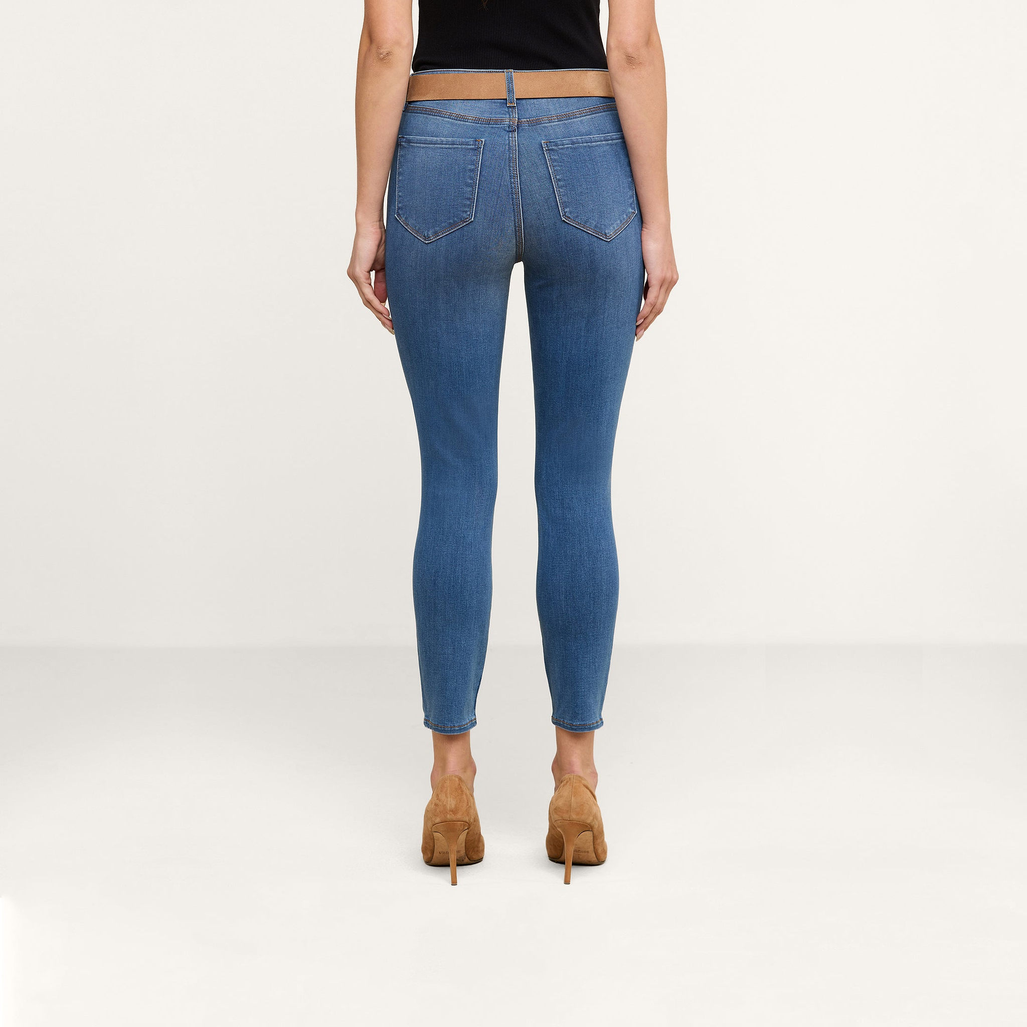 Si vede una persona di spalle, in piedi su uno sfondo beige a tinta unita, che indossa i jeans skinny corti Margot in denim elasticizzato e scarpe con tacco alto color cuoio.