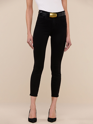 A person in a white sleeveless top, Margot Cropped Skinny Jean in black stretch denim, a black belt with a large gold buckle, and black heels stands against a beige background with arms relaxed at their sides.