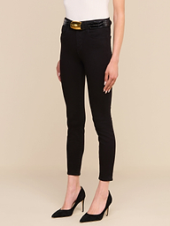 Wearing the Margot Cropped Skinny Jean in black, styled with a white sleeveless top, a black belt featuring a gold buckle, and black pointed-toe high heels. The person is standing against a plain white background with only the lower body visible.