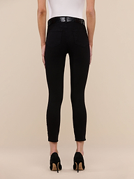 Person standing facing away, wearing a white top, the Margot Cropped Skinny Jean in black high-rise stretch denim, a black belt, and black high-heeled shoes against a plain white background.