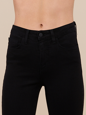 A close-up of a person’s midsection in Margot Cropped Skinny Jean, a high-rise black stretch denim with front pockets, belt loops, and button closure. The background is plain beige.