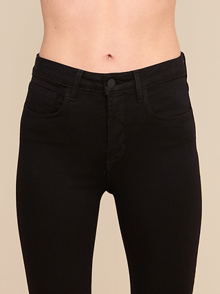 Eine Person, die die „Margot Cropped Skinny Jean“ aus schwarzem Stretch-Denim trägt, abgebildet von der Taille bis zu den Oberschenkeln vor einem einfarbigen beigen Hintergrund.