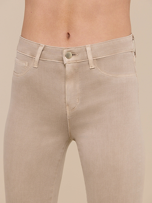 Close-up of a person wearing the Margot Cropped Skinny Jean in beige stretch denim, featuring a contoured waistband, front button, belt loops, and pockets. Focus is on the waist and upper thighs against a plain neutral background.