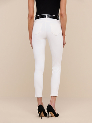 A person in Margot Cropped Skinny Jeans, a black belt, black sleeveless top, and black high heels stands facing away from the camera against a plain beige background.