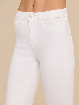 A close-up of a person wearing the Margot Cropped Skinny Jean in white stretch denim with front pockets and button closure, shown from waist to mid-thigh against a beige background.
