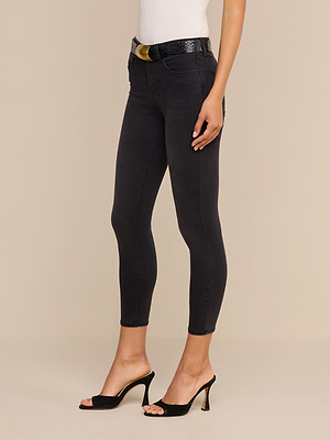 Una donna che indossa i jeans skinny corti Margot in denim elasticizzato con fascia in vita sagomata, un top bianco senza maniche, una cintura nera con fibbia dorata e mules neri con tacco alto, in piedi su uno sfondo beige.