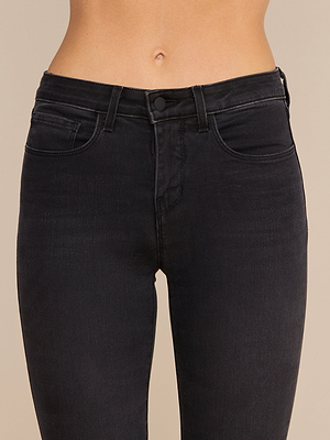 Eine Person trägt die „Margot Cropped Skinny Jean“ – eine schwarze Jeans mit hoher Taille, einem figurbetonten Bund und Vordertaschen –, die aus Stretch-Denim gefertigt ist und vor einem einfarbigen Hintergrund von der Taille bis zur Mitte des Oberschenkels zu sehen ist.